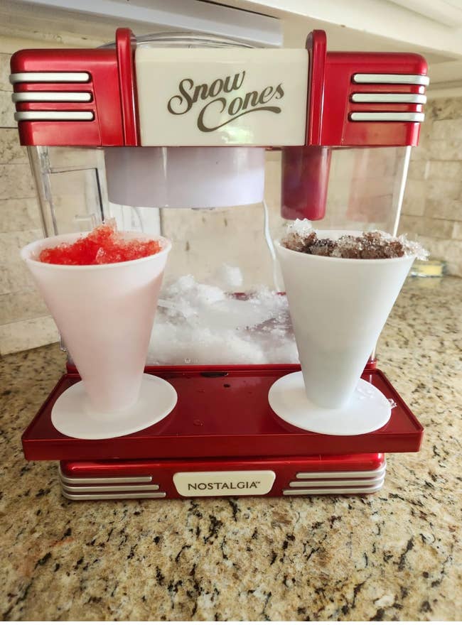 Nostalgia snow cone maker on a counter with two cones; one red and one brown