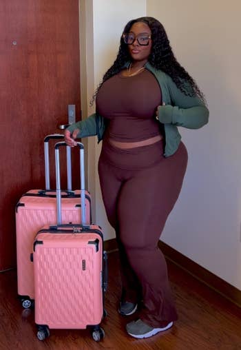 A reviewer is dressed in a maroon lounge set with two pink suitcases