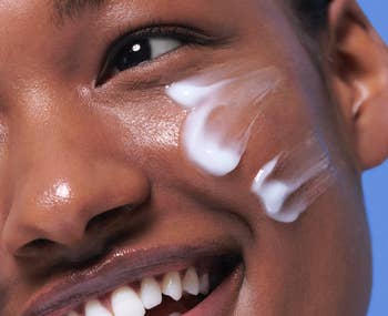 Close-up of a smiling person applying cream to their cheek, illustrating skincare application