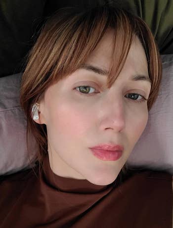 Person lying down, wearing a brown top and earbuds. Relaxed expression. Featured in a shopping section article