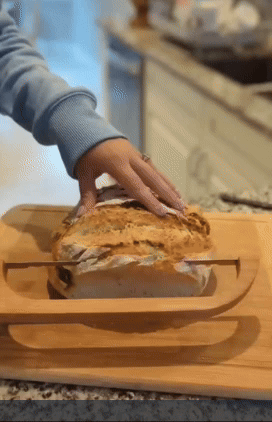 Person slicing freshly baked bread with a bow cutter knife