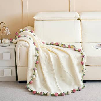 A cozy knitted blanket with a floral border draped over a cream sofa in a living room setting, creating a warm and inviting atmosphere