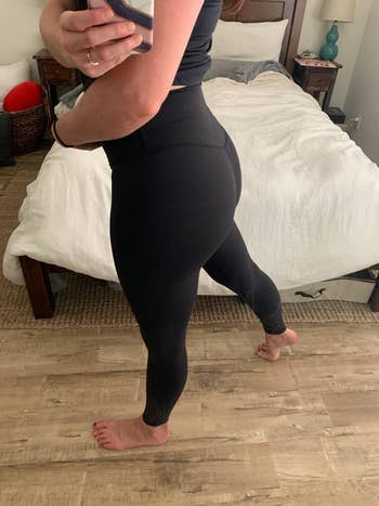 Person wearing black leggings taking a mirror selfie in a bedroom setting