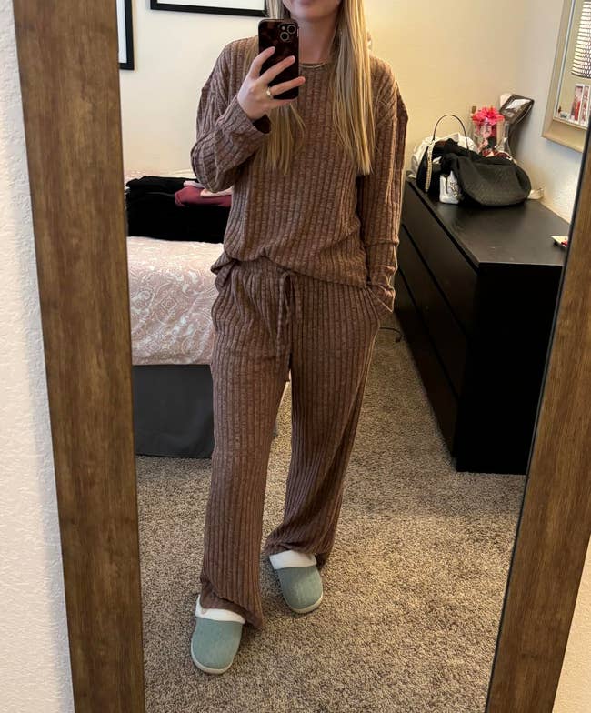 Person wearing a casual, ribbed lounge set and slippers, taking a mirror selfie in a bedroom with a dresser and a handbag in the background