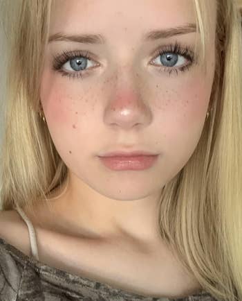 Person with light hair and freckles, wearing a brown top, looking directly at the camera
