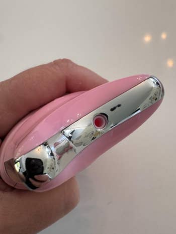 Hand holding a compact, pink electronic device with a sleek metallic button, suitable for beauty or personal care routines