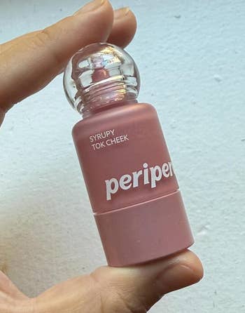 Hand holding a bottle of Peripera Syrupy Tok Cheek tint, featuring a unique round cap design