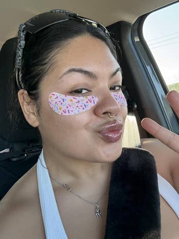 Person with playful eye patches and sunglasses on head poses with peace sign in a car