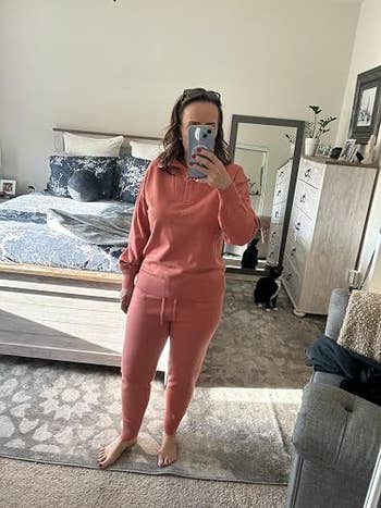 Person in a cozy casual outfit taking a mirror selfie in a bedroom