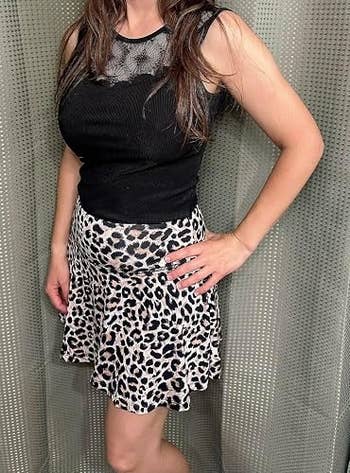 Person in a sleeveless black lace top and a leopard print skirt poses with one hand on hip