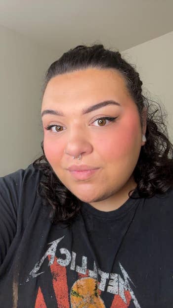 Person with curly hair and a septum piercing wearing a graphic T-shirt, looking at the camera