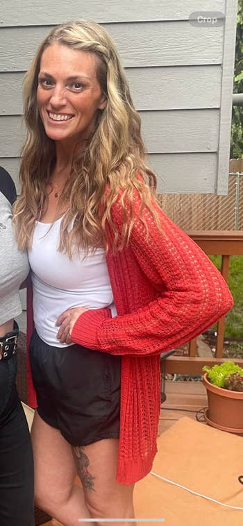 Person in stylish casual wear with a knitted cardigan, tank top, and shorts, posing outdoors on a deck