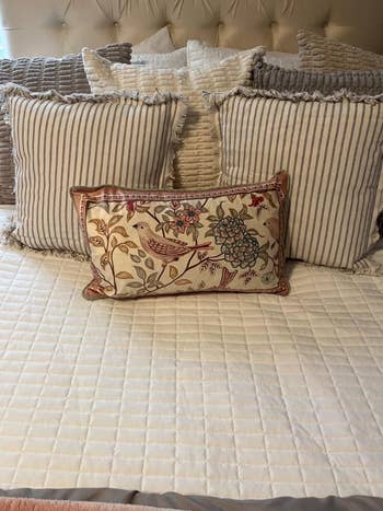 Decorative throw pillows with various patterns are arranged on a neatly made bed with a quilted blanket