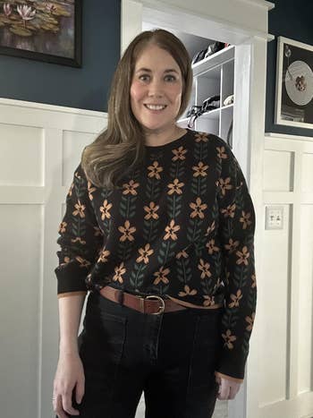 Person wearing a sweater with floral patterns and jeans, standing in a stylishly decorated room
