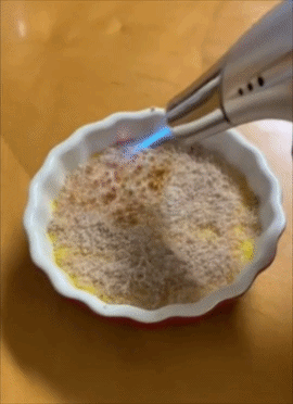 A torch caramelizes sugar on a dessert in a round dish, creating a crispy topping, perfect for gourmet kitchen tools shopping
