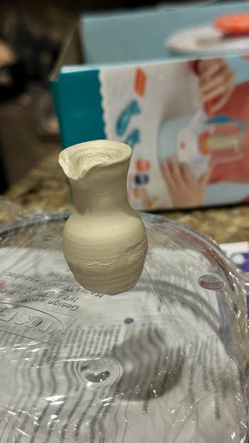 Miniature clay vase on a plastic lid with a pottery kit box in the background