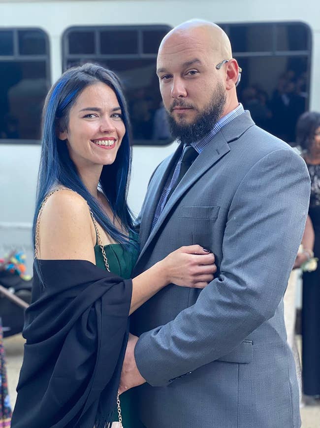 A person in a stylish black wrap and a man in a formal gray suit pose together, both smiling confidently at a social event