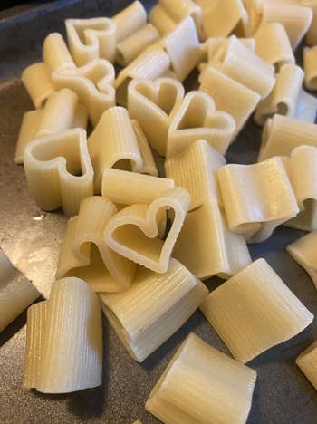 Heart-shaped and cylindrical pasta pieces are displayed on a metallic surface