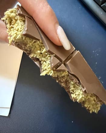 A hand holding a chocolate-covered wafer, with a crispy textured filling visible, broken into pieces