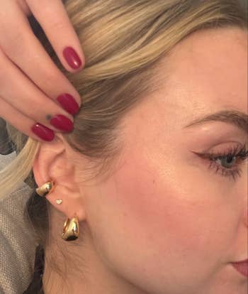 Close-up of person wearing gold huggie earrings with polished nails and winged eyeliner, highlighting jewelry for a shopping feature