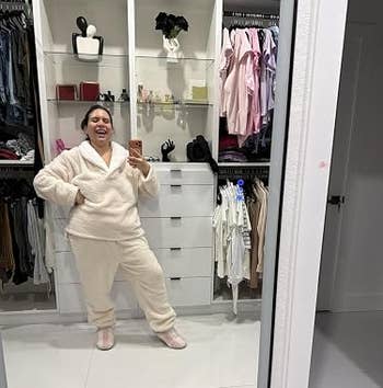 Person happily posing in cozy, plush loungewear in a stylish walk-in closet with organized clothes and accessories