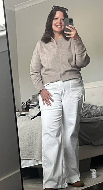 A person takes a mirror selfie wearing a casual, cozy outfit with a sweater and wide-leg pants, standing in a bedroom