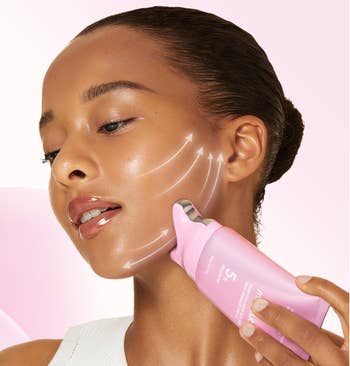A person applies skincare serum to their cheek using a pink bottle, with white arrows illustrating a lifting effect