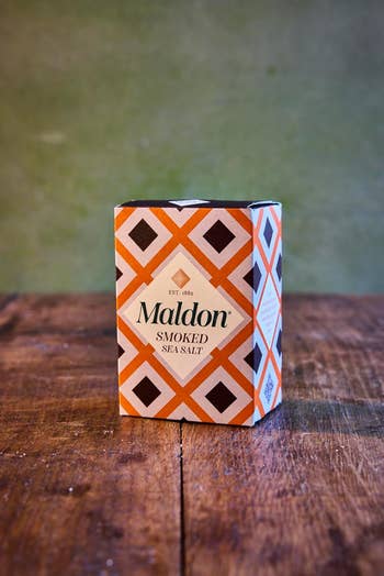 Maldon Smoked Sea Salt box with a geometric design, placed on a wooden surface. Ideal for seasoning and culinary use