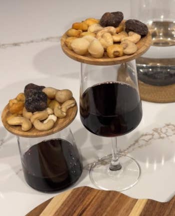 Two wine glasses on a table with wood trays on top, loaded with assorted nuts and chocolates. Suitable for a food and wine shopping feature
