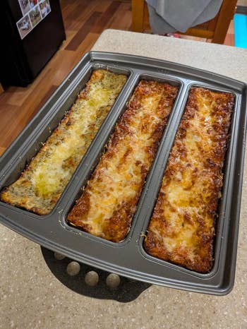 Three loaves of baked lasagna sit in a segmented baking pan on a kitchen counter