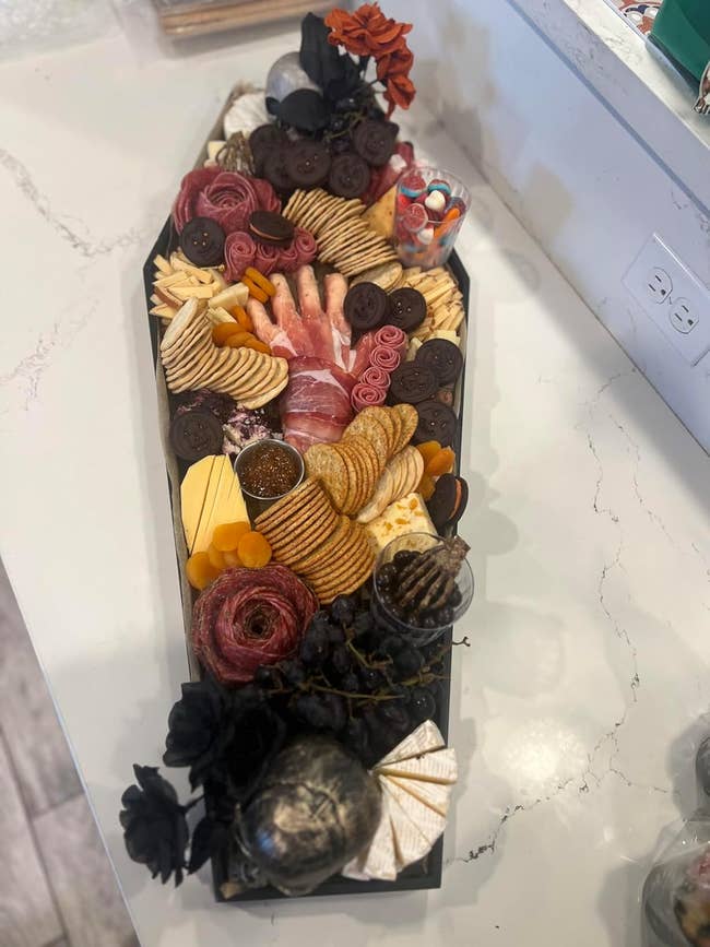 A coffin-shaped charcuterie board with various meats, cheeses, crackers, and garnishes 