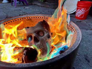 A skull-shaped fire log is burning with bright multicolored flames in a fire pit