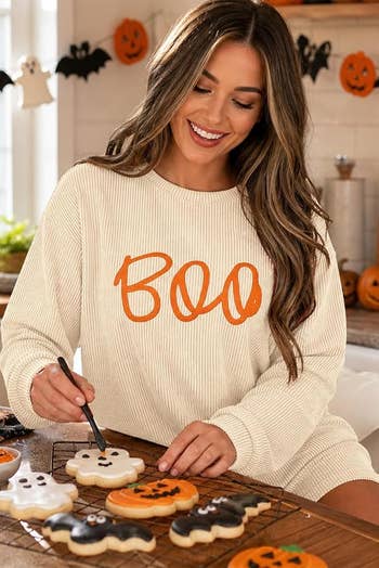 Person decorating Halloween-themed cookies, wearing a ribbed sweater with 