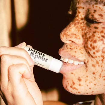 Person applying Poppy & Pout lip balm, smiling, close-up shot, showcasing product in use