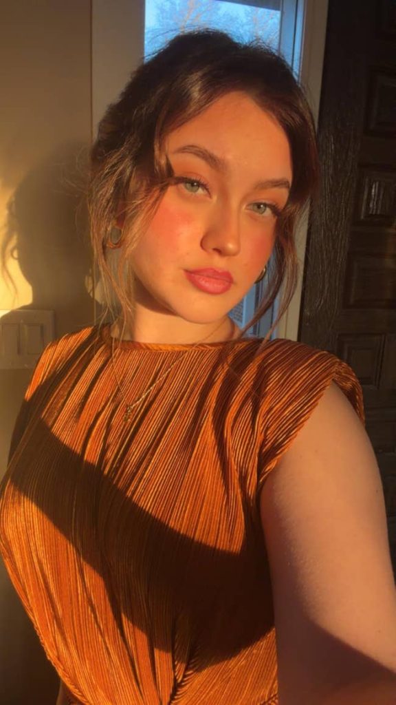 Person in pleated, sleeveless dress, posing with soft lighting