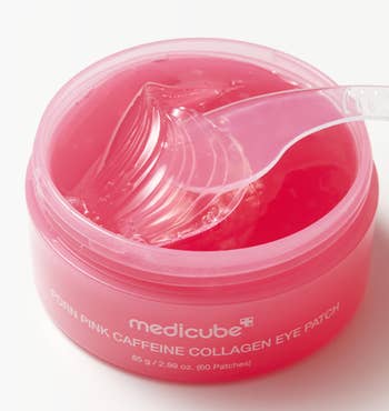 Open tub of medicube's Pore Pink Caffeine Collagen Eye Patch with a translucent applicator scooping a patch