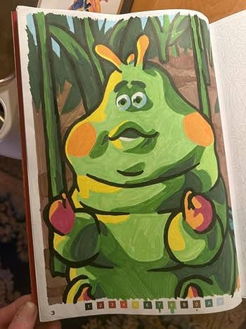 Cartoon character resembling a green caterpillar with orange cheeks, sitting on a background of large leaves