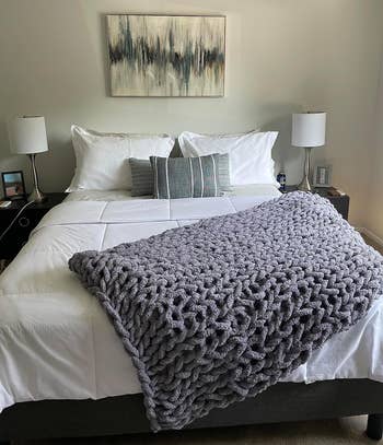 A grey knitted blanket laid across a bed.