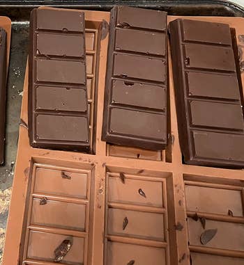 Chocolate bars setting in molds on a metal tray. Small chocolate pieces scattered around the molds