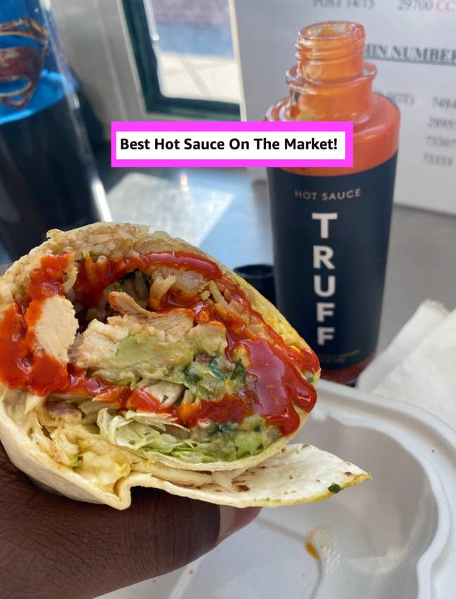 A person holds a burrito with chicken, avocado, and hot sauce. A bottle of Truff hot sauce is nearby with a caption declaring it the best on the market