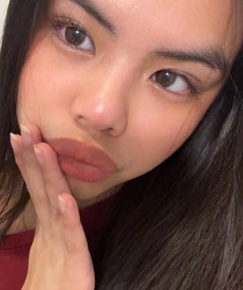 Person touching face, showcasing natural makeup look with eyeliner and lipstick