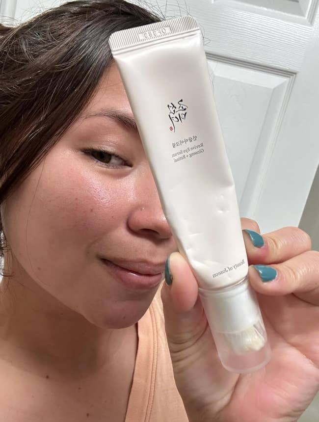A person holding a tube of facial cleanser close to their face, showing smooth skin