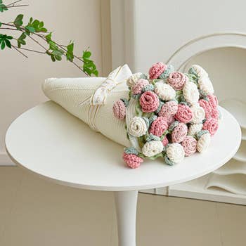 Crocheted bouquet of pastel roses on a white table, wrapped in fabric with a ribbon. Perfect for decorative home accents or gift ideas