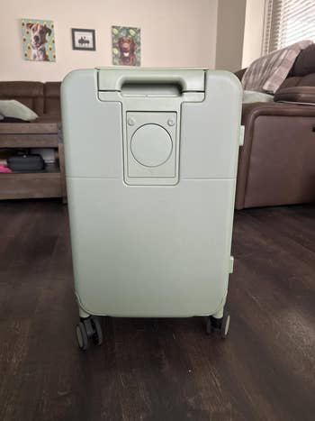 A sleek, modern wheeled suitcase with a minimalist design displayed in a stylish living room setting