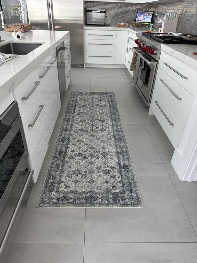 Kitchen with white cabinets, modern appliances, and a patterned runner rug positioned between the countertops