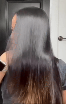 Person brushing straight, glossy hair in front of a mirror, highlighting hair care routine