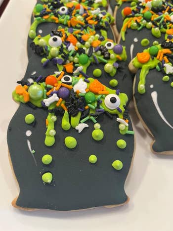Halloween-themed cookies covered in black icing, colorful sprinkles, and Halloween decorations like eyes and bones