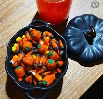 Halloween-themed candy corn and pumpkin candies in a black pot next to a red drink on a wooden table