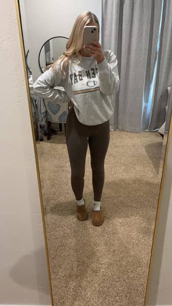 Person taking a mirror selfie wearing a sweatshirt, leggings, and slippers