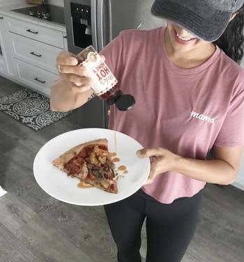A reviewer drizzling hot honey on pizza